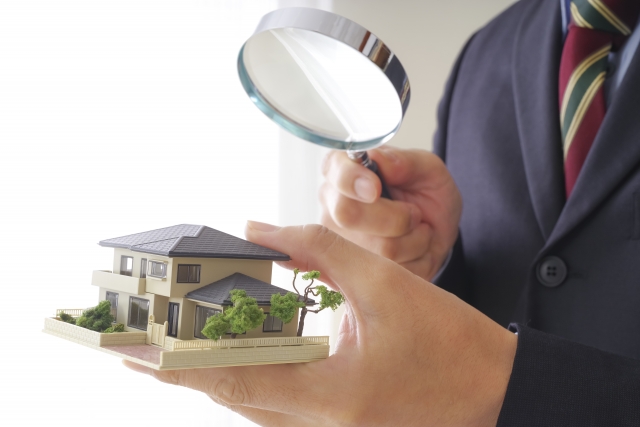 家の模型を虫眼鏡で見ている男性