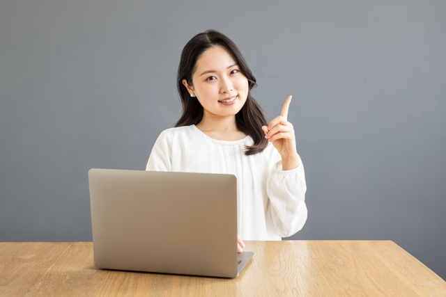 パソコンの前で人差し指を建てる女性
